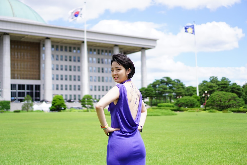 A young Korean woman in a low backed purple dress with tattoos across her back 