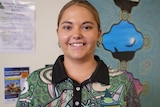 A young womanl with brown eyes, blonde and brown hair, wearing a colourful shirt smiles at the camera.