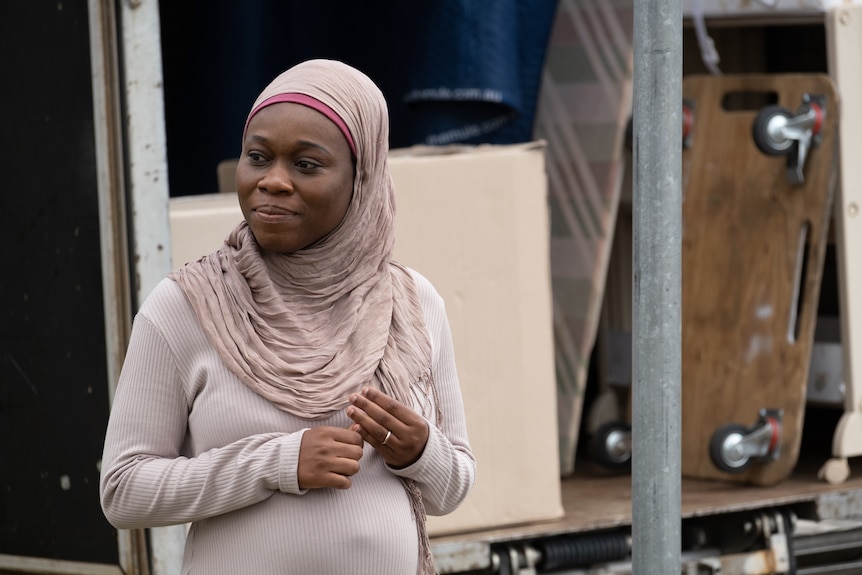 Actor Bolude Watson in a scene from the film Hearts and Bones, a pregnant woman wearing a hijab, moving truck in the background