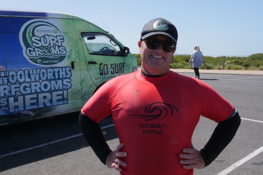 A man smiling in red rashie with Go Surf van behind him