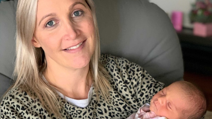 Woman with blonde hair holds newborn baby in her arms