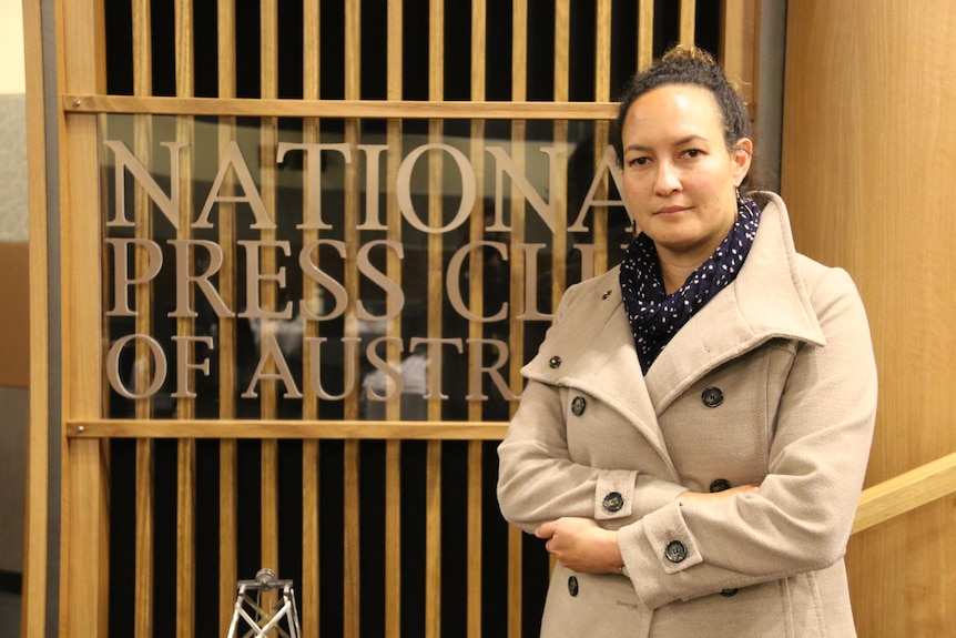 Fiona Cornforth standing with her arms crossed in front of the National Press Club of Australia sign.