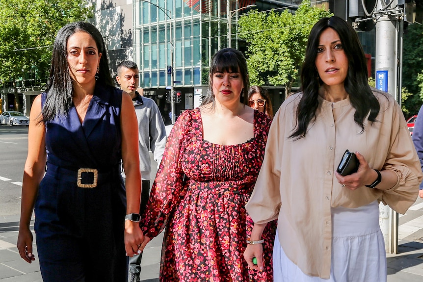 Elly Sapper, Dassi Erlich and Nicole Meyer hold hands as they walk across a CBD road in Melbourne's courts precinct.