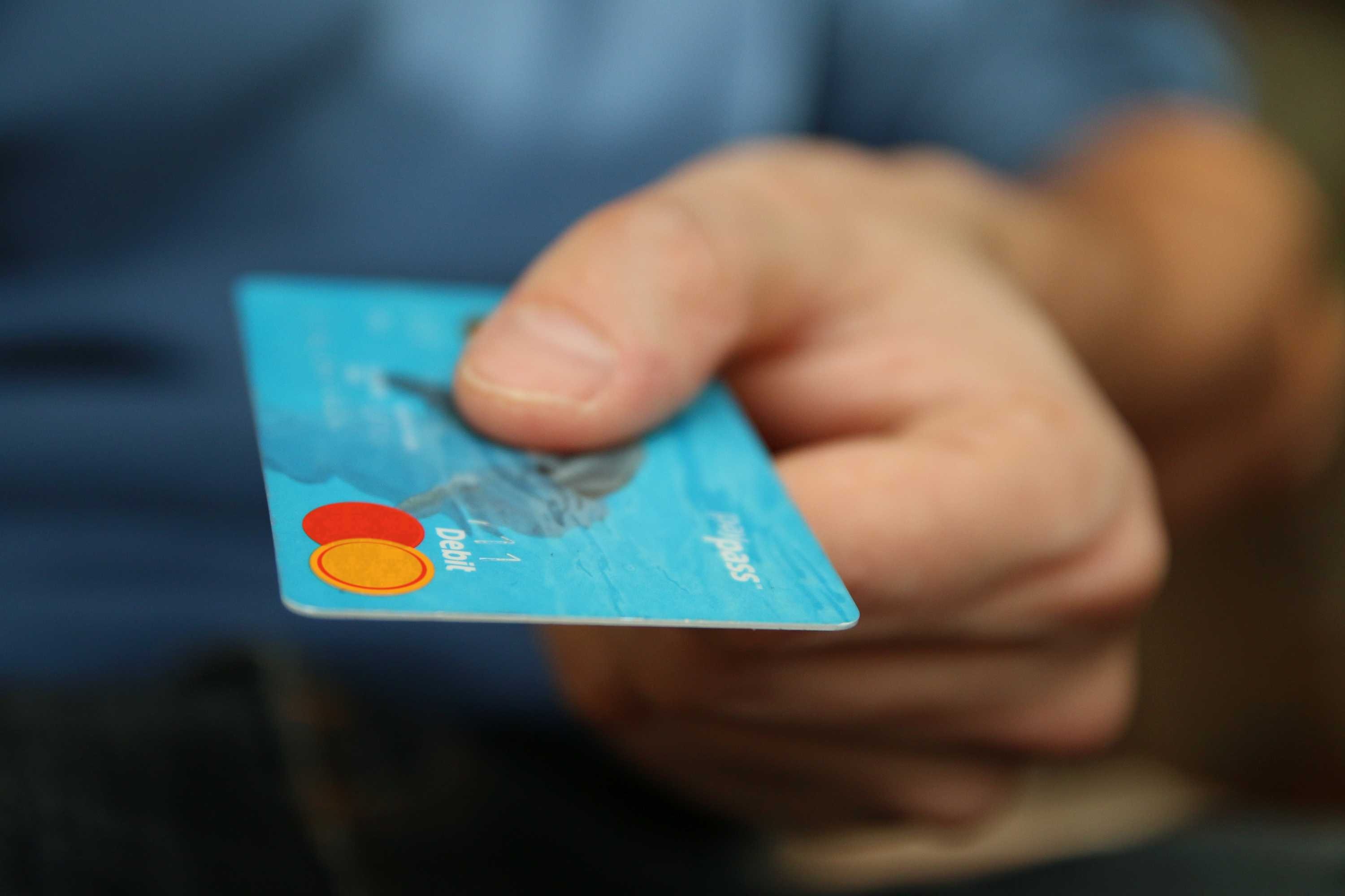 A hand holding a credit card out towards a recipient.