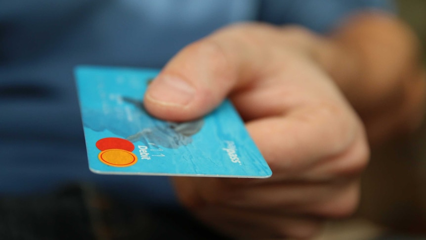 A hand holding a credit card out towards a recipient.