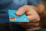 A hand holding a credit card out towards a recipient.