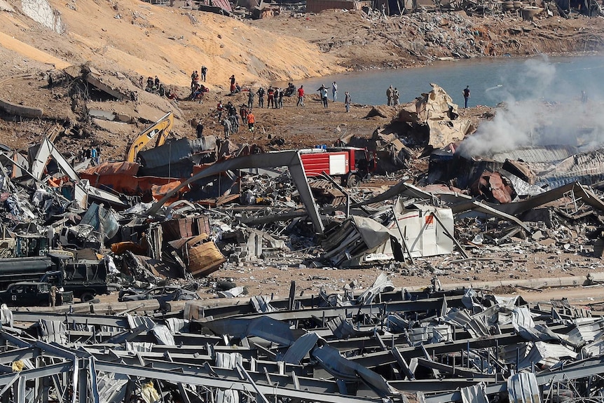 A pile of rubble with smoke rising above it as rescue workers and security officers work nearby.