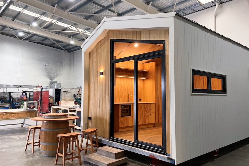 A white tiny home with wooden front and black windows with a wooden table and chairs outside 