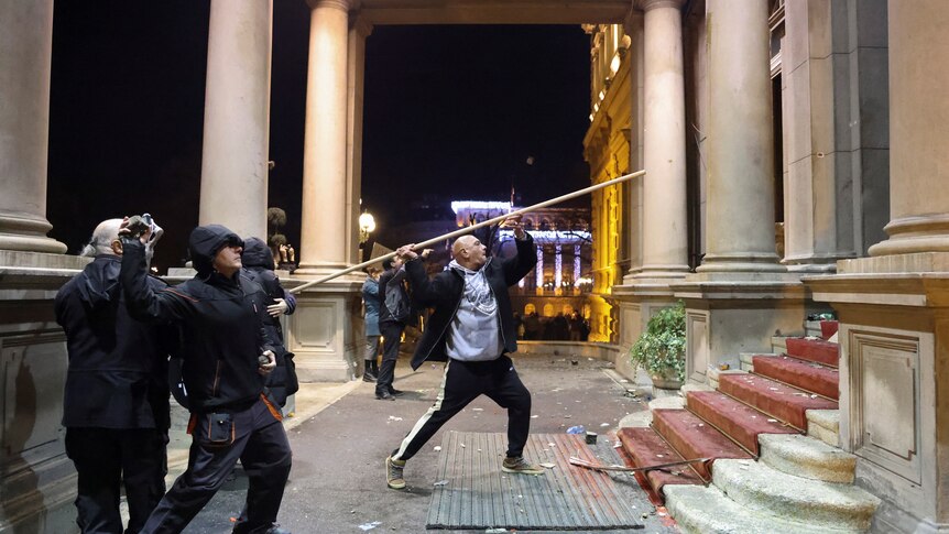 A man with a big stick makes his way toward the building 