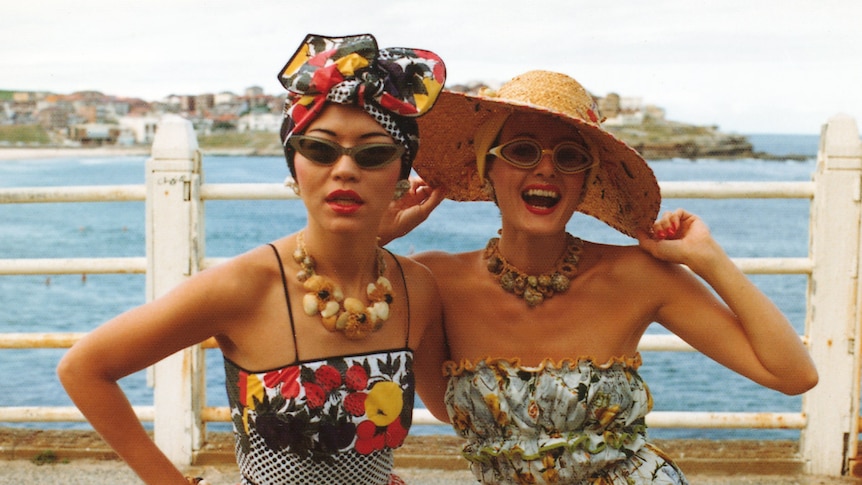 Jenny Kee and Linda Jackson in the 1970s on a pier at the beach wearing their signature colourful clothing.