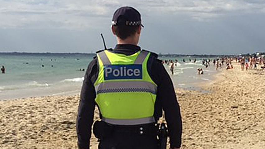 A police officer walks on a beach.
