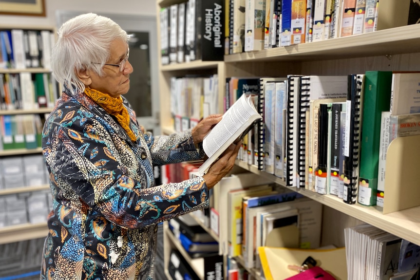Aboriginal elder in library archives reading book in the Aboriginal history section wearing colourful shirt