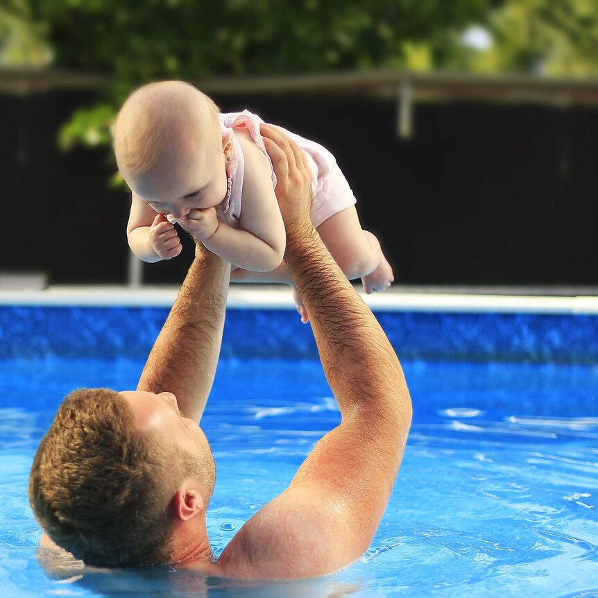 a father  plays with a baby in a swimming pool