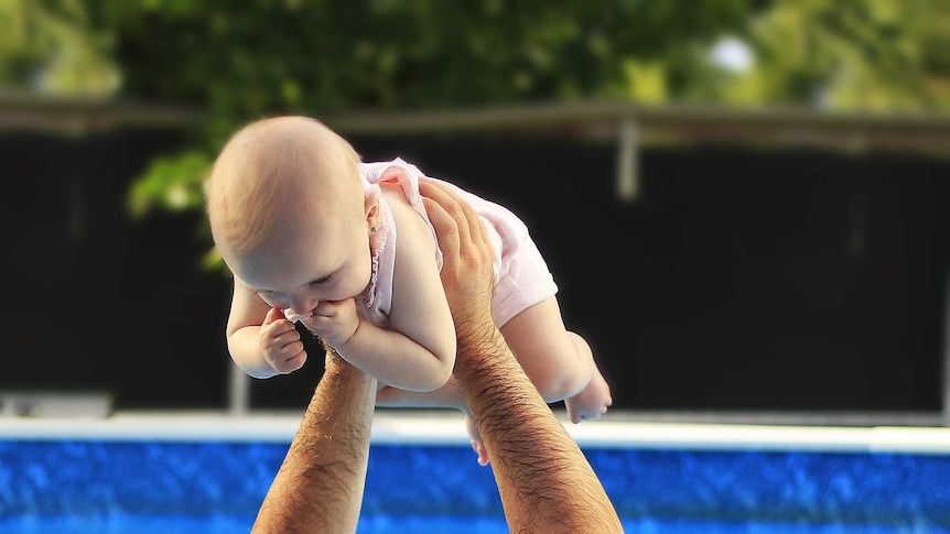 a father  plays with a baby in a swimming pool