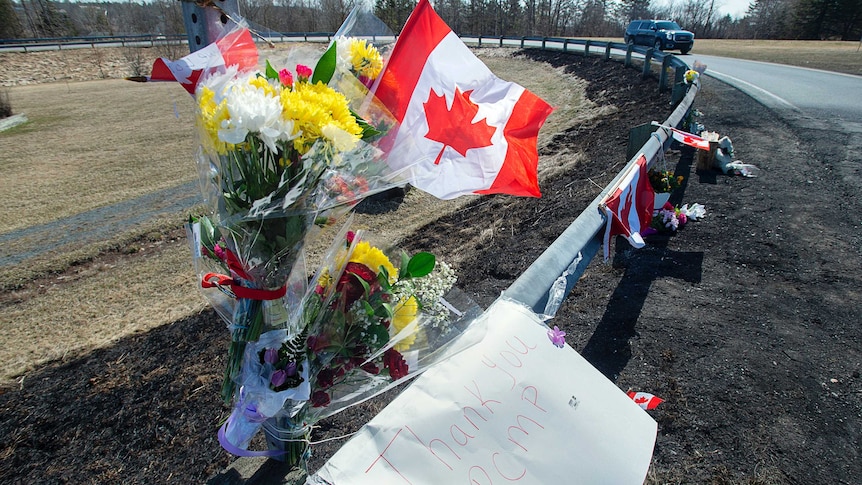 Flowers and a Canadian flag are tied by the road side.