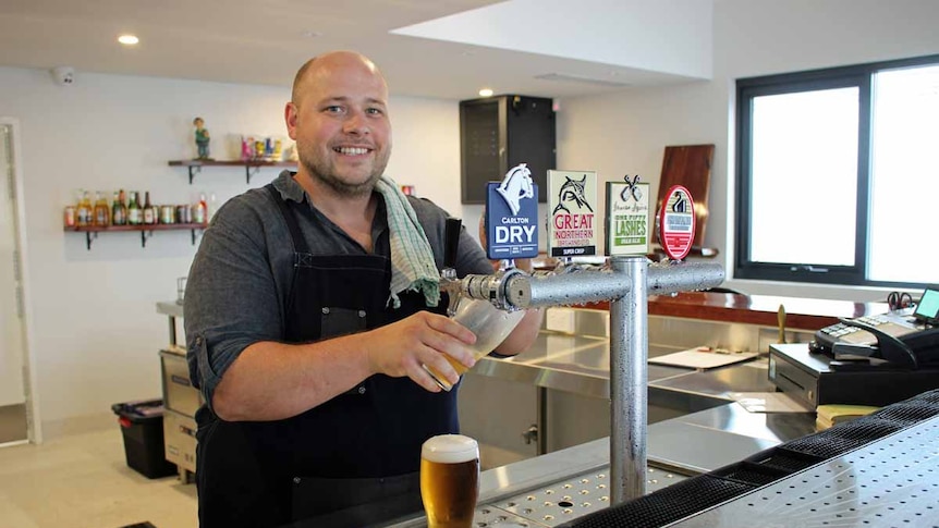 A man wearing an apron stands behind a bar pulling a fresh beer into a glass.