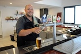 A man wearing an apron stands behind a bar pulling a fresh beer into a glass.