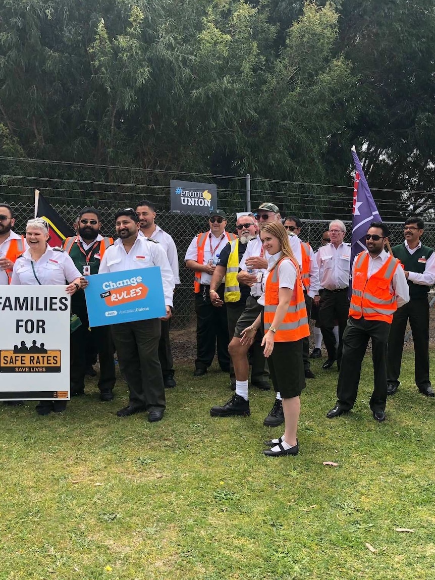 A group of bus drivers in uniform protesting outside a bus depot.