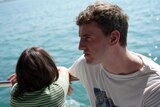 A young girl facing out to the water and man in his late 20s in a white shirt sitting on a boat