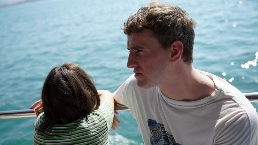 A young girl facing out to the water and man in his late 20s in a white shirt sitting on a boat
