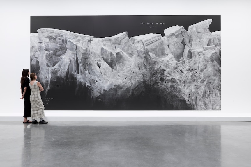 Two people stand observing a large canvas featuring a black and white image, hanging in a gallery.
