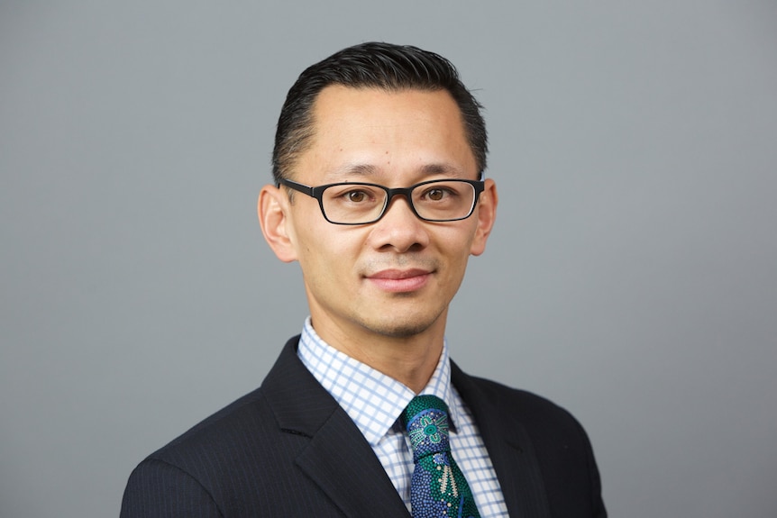 A man in a suit and glasses stands against a blank background