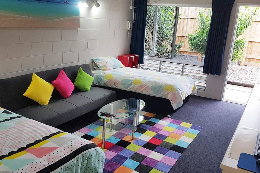 A photo of inside a student lodge with beds, a couch and colourful pillows.