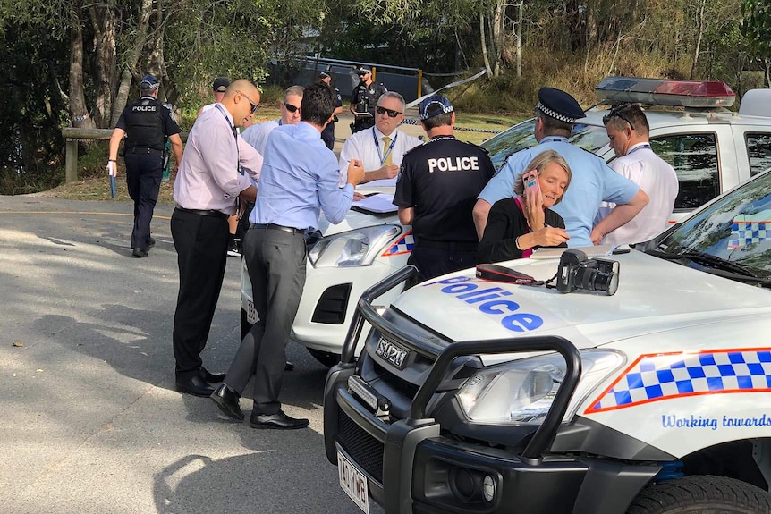 Police officers leaning on the bonnets of police cars at a crime scene