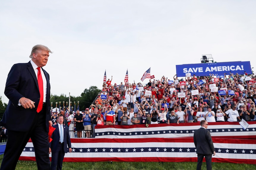 Donald Trump wchodzi na podium ze swoimi zwolennikami w tle