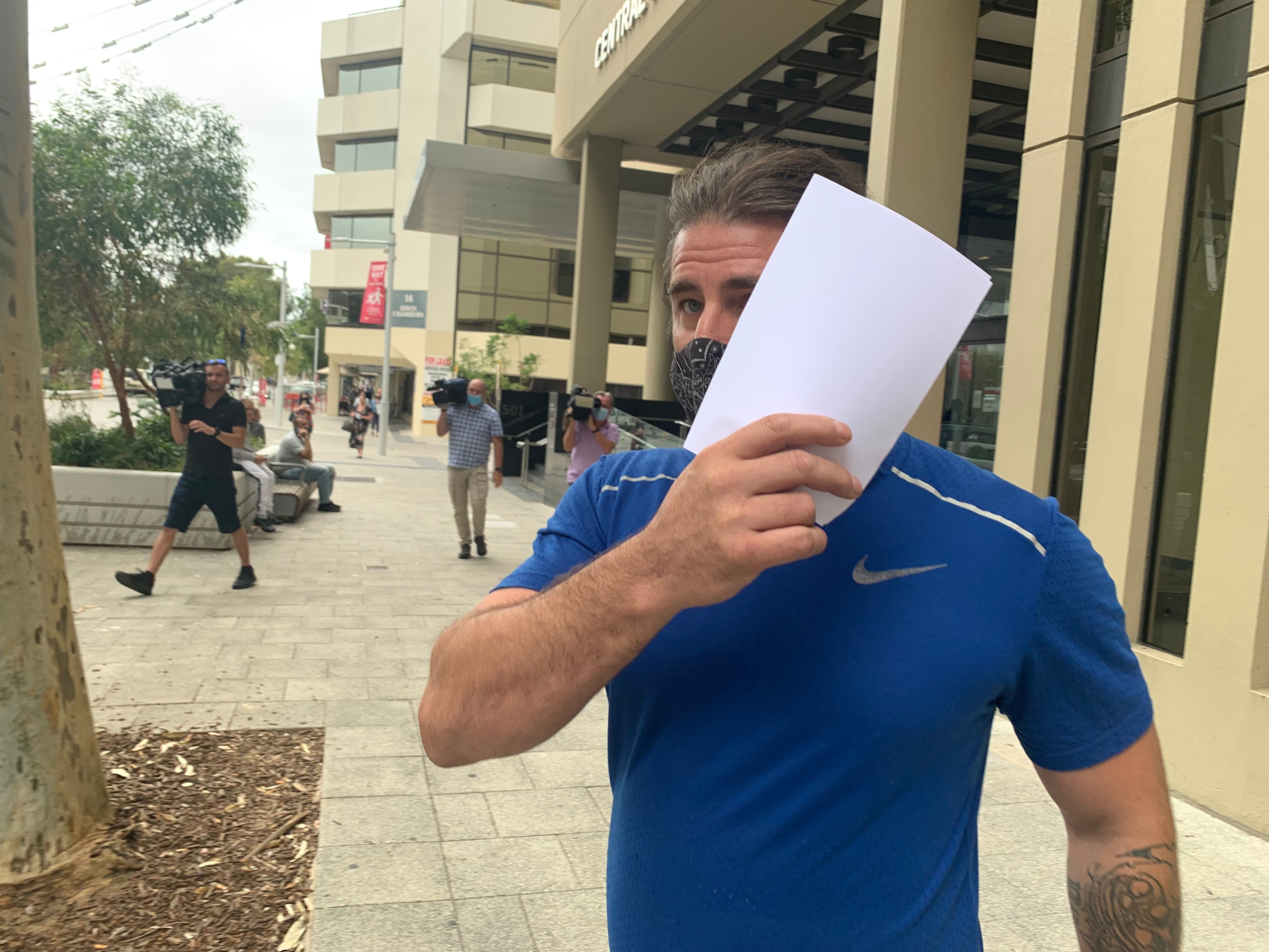 a man in a blue shirt covering his face with a piece of paper.