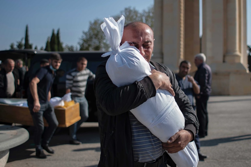 Timur Haligov, a father, embraces the body of his 10-month-old daughter at her funeral. She was killed in Armenian shelling.