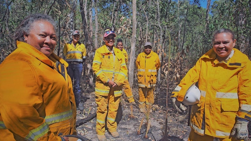 Group of women standing in bushland wearing yellow fire jackets and pants.