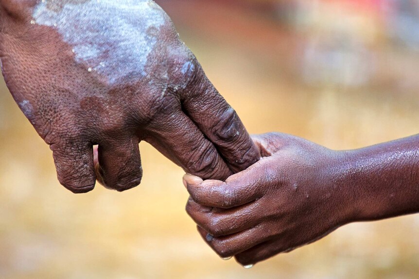 Close up image of Aboriginal father and son holding hands.