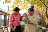 Two women look down at a baby being held by one 