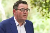 Victorian Premier Daniel Andrews wearing a blue suit jacket and talking in a green leafy location.