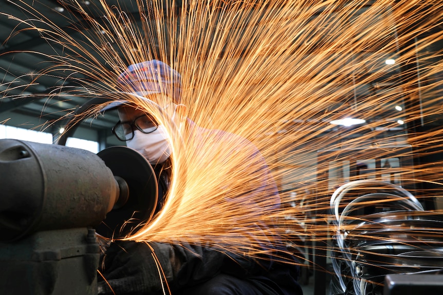 A worker wearing a face mask works on a production line manufacturing bicycle steel rims in China.