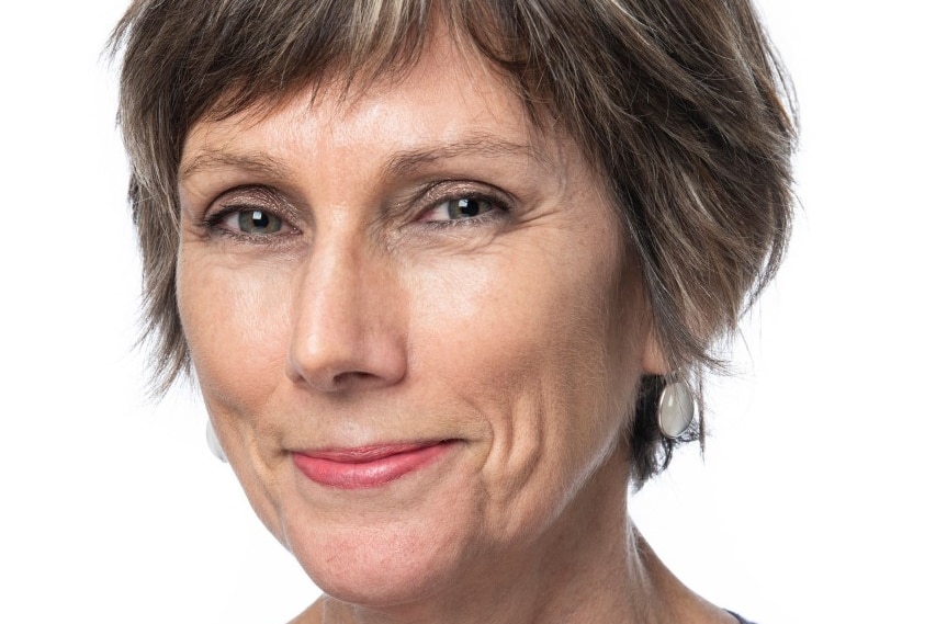 A headshot of a woman smiling with short brown and grey-flecked hair. 