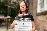 A young woman holding a clapper board