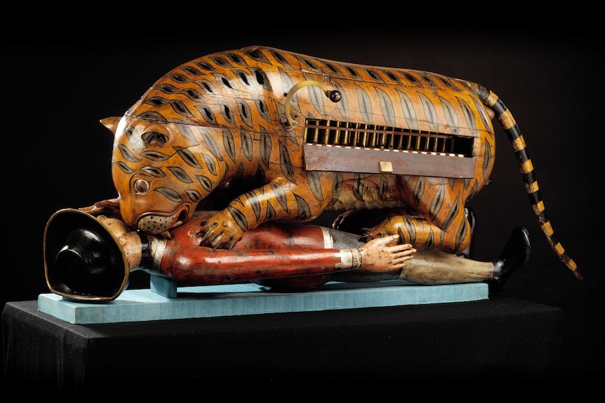 A wooden automaton of a tiger mauling a British soldier. The side of the tiger is open showing organ-like pipes.