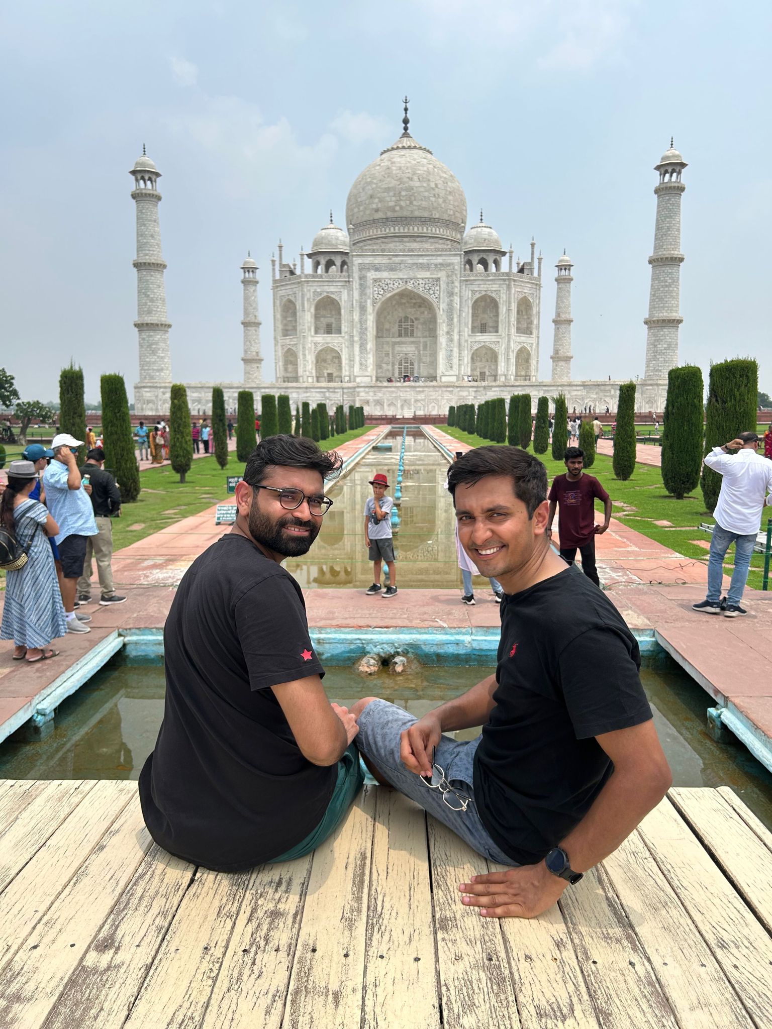 Two smiling men sit in front of the Taj Mahal, looking back at the camera.