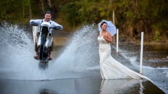 Gavin drives a motorbike through a puddle past his wife in her wedding dress.