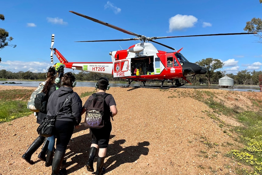 Four people with headphones on walk up a small bank to a red and white helicopter.