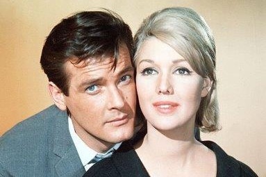 Colour image of Roger Moore, with dark hair, with face pressed close to Annette Andre, with blonde hair. Both smile slightly.