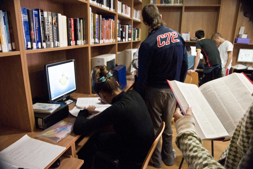 A group of young people holding books and looking at computers