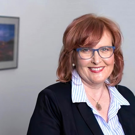 Dr Karen Price smiling and wearing purple glasses in an office.