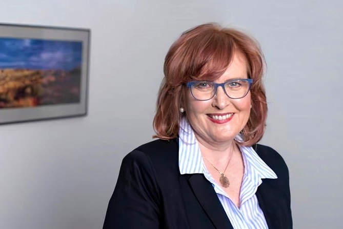 Dr Karen Price smiling and wearing purple glasses in an office.