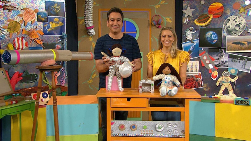 Presenters Alex and Rachael stand with Play School toys on the set decorated with images and artworks from sea and space.