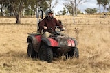 A farmer, wearing a helmet, rides a quad bike with his dog on the back