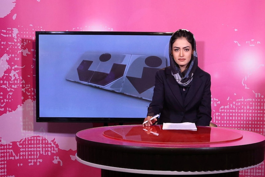 TV presenter behind desk in a studio.