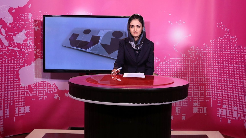 TV presenter behind desk in a studio.